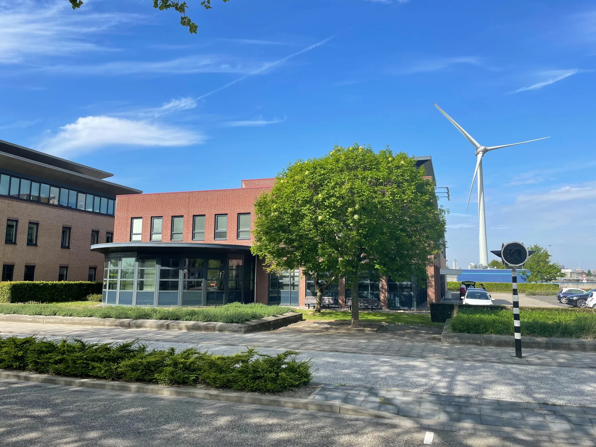 Kantoorgebouw aan de Rivium 4e Straat met een windturbine op de achtergrond op een zonnige dag.